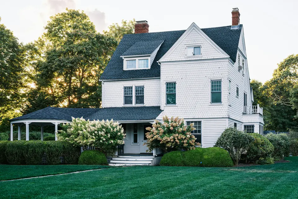 Well-kept white house with a dark roof, blue hydrangeas and a freshly mown lawn