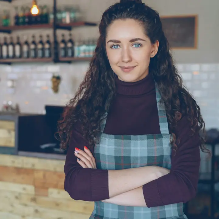 Coffee shop owner standing in her shop with her arms crossed, smiling