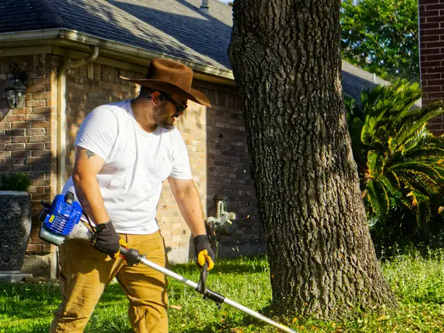 Landscaper trimming the lawn in front of a brick home
